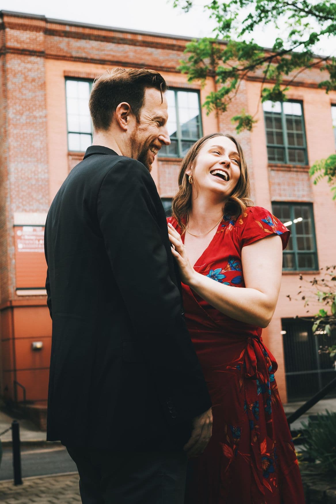 A couple laughing together on a city street, dressed for an evening out.