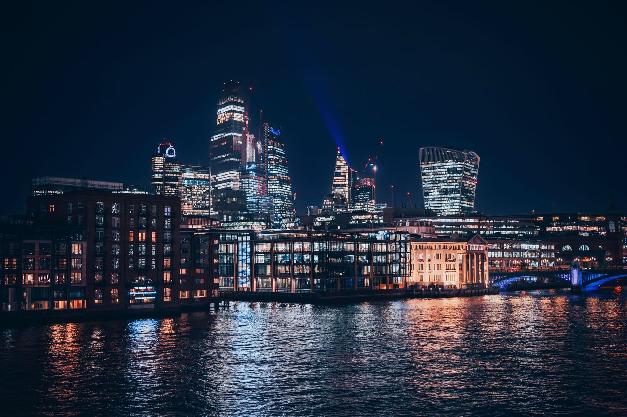 The City of London skyline reflected in the Thames at night.